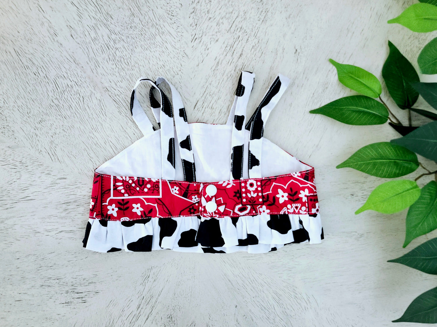 Back of black-and-white patterned top with a red bandana design on a light wooden surface with green leaves.
