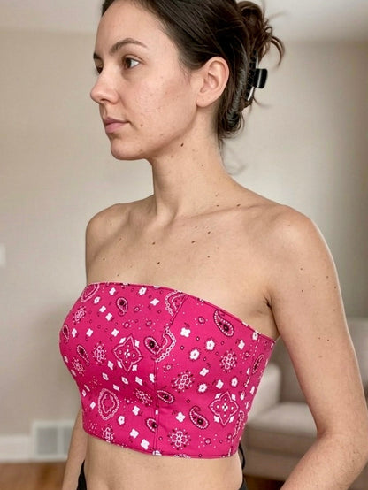 Woman wearing a pink bandeau top with a pattern in a room.