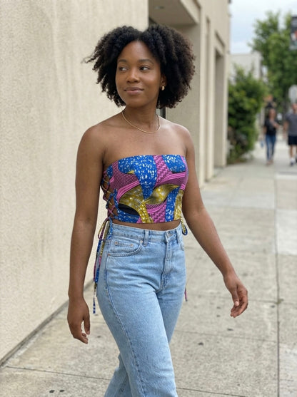 Woman wearing a colorful African Print strapless top and blue jeans on a city street.
