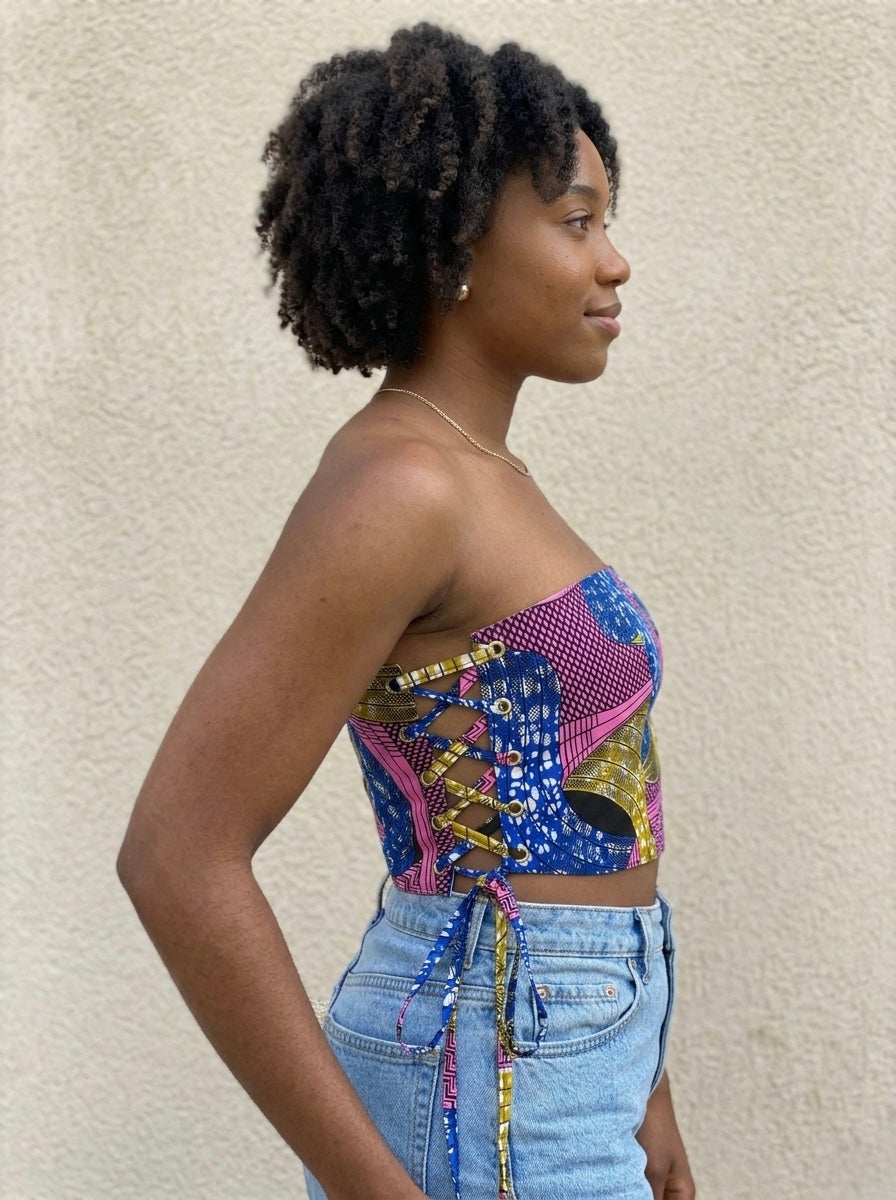 Woman wearing a African print colorful patterned top and blue jeans against a beige wall