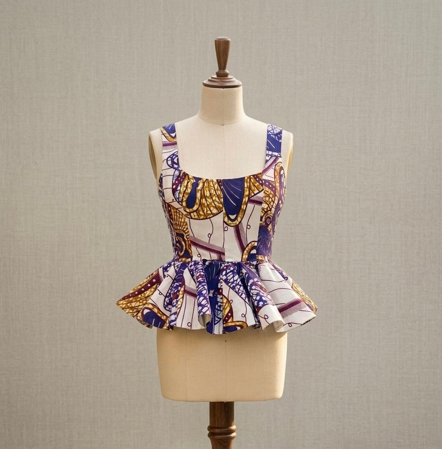 A sleeveless top with a square neckline and peplum hem, featuring an African wax print pattern in purple, gold, and white, displayed on a cream dress form mannequin against a neutral textured background.