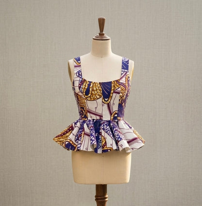 A sleeveless top with a square neckline and peplum hem, featuring an African wax print pattern in purple, gold, and white, displayed on a cream dress form mannequin against a neutral textured background.