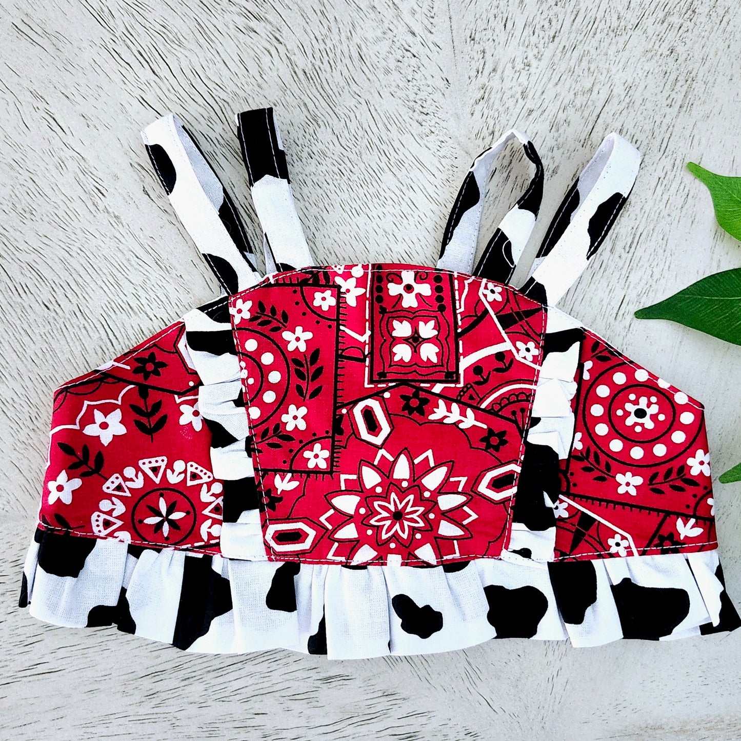 Red, black, and white Western Bandana-patterned and Cow print Crop top on a wooden surface with green leaves.